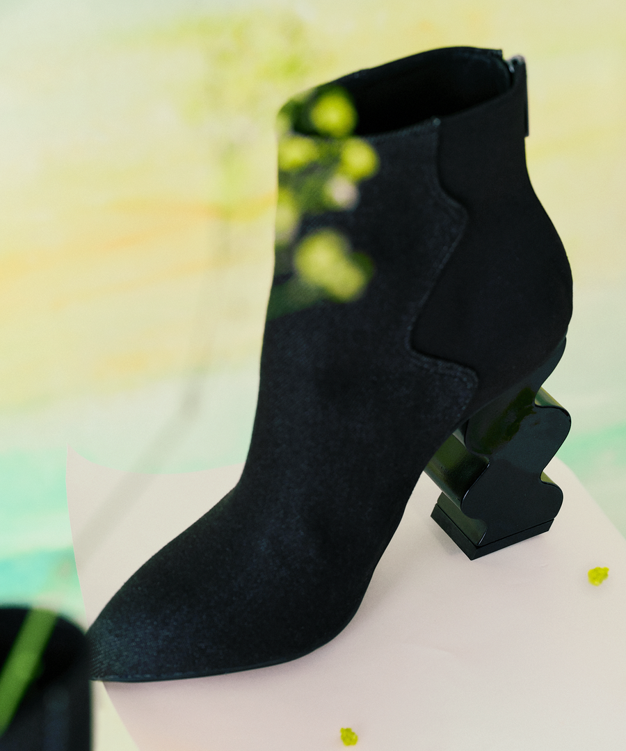 Black INES denim ankle boot with iRi's unique Dancing heel design on a colorful abstract background