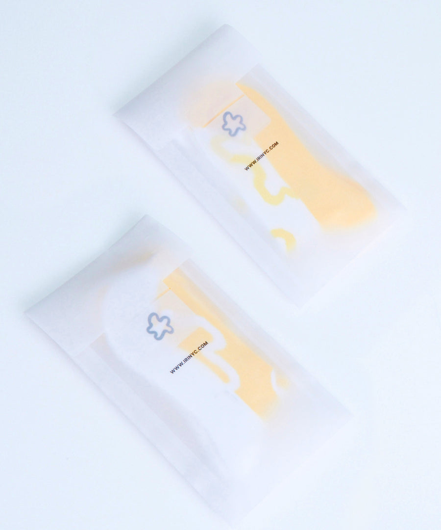 Yellow and white socks with iRi iconic abstract patterns on a pale grey background, inside iRi branded paper pacakging