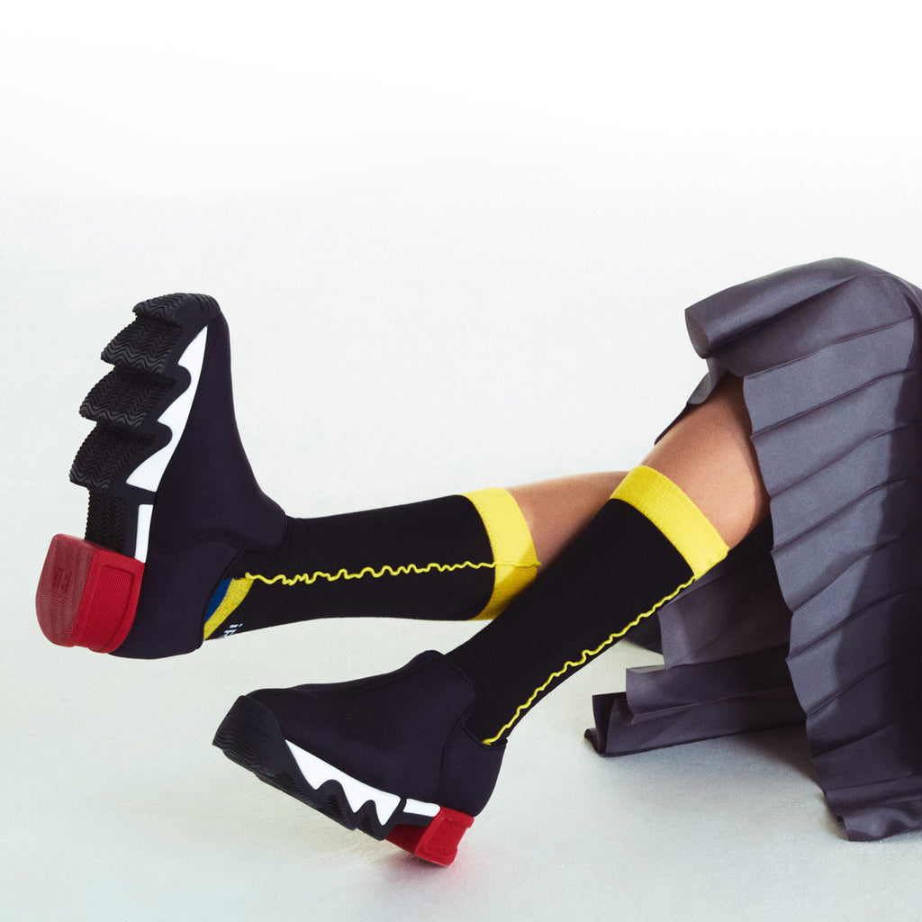 A model wearing black pleated long pants with WES Black Red Low Top Sneaker, styled with knee-length DANCING QUEEN burgundy cotton socks